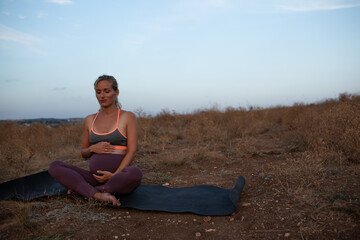Fototapeta na wymiar Pregnant woman makes yoga exercise outdoor in the meadow dry grass