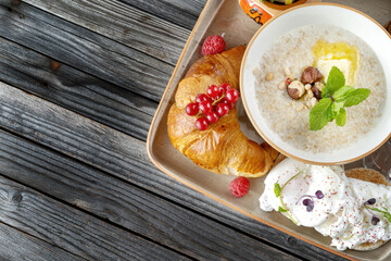 Breakfast. Fruits, croissants, porridge, poached eggs. On rustic dark wooden table.