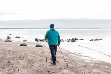 Nordic walking, rear view on elderly aged caucasian european men walks with canes near lake. Sports exercises for healthy spine and joints, therapy for health. view from back.