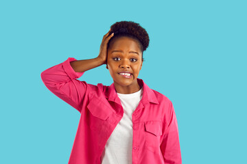 Confused puzzled african american young woman in pink jacket on blue background. She is touching...