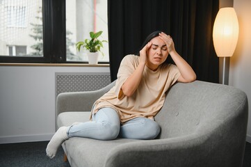 Obraz premium girl holding her head, woman has a headache. sad female sitting on couch