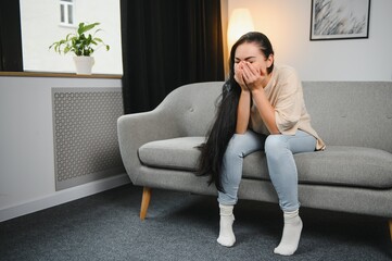 Depressed sad attractive woman crying on sofa couch at home feeling lonely tired and worried suffering depression in mental health, loneliness and isolation concept. Psychology, solitude and people.