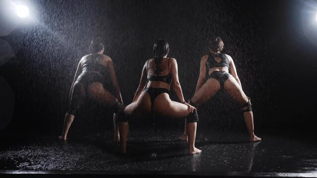 Three sexy women in mesh tights dancing under water droplets