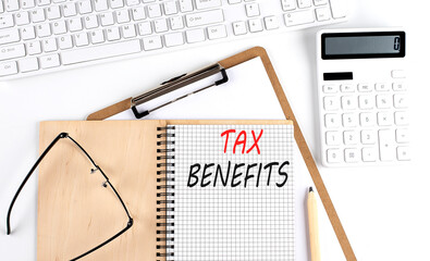 Notebook with the word TAX BENEFITS with keyboard and calculator on the white background