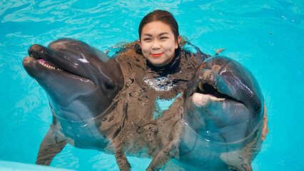 Cute woman smiling with two dolphins in the swimming pool.