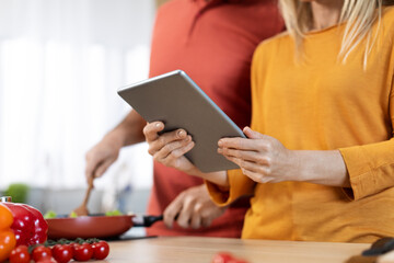 Unrecognizable spouses cooking healthy dinner, checking recipes online, using tablet