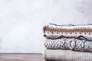 Stack of cozy knitted sweaters on a wooden table. Faded retro style image. Space for text. Warm...