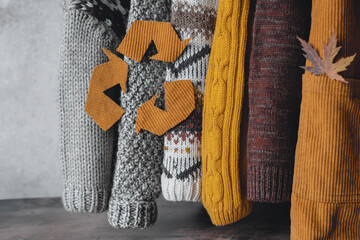 Clothing recycling. Sleeves of knitted sweaters in an autumn palette hang on a gray background. used sweaters. Ecological and sustainable fashion. 