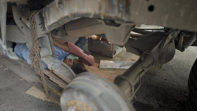 Old Traditional Asian Mechanic Repairing A Car Using A Blowtorch And A Protective Face Mask