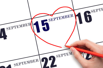 A woman's hand drawing a red heart shape on the calendar date of 15 September . Heart as a symbol...
