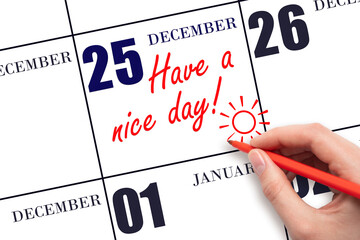 The hand writing the text Have a nice day and drawing the sun on the calendar date December 25