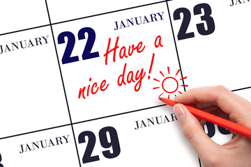The hand writing the text Have a nice day and drawing the sun on the calendar date January 22