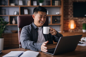 Glad adult chinese man ceo manager work with laptop with cup of drink and talking with client