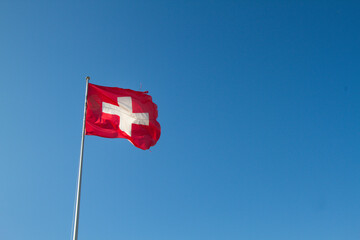 Switzerland flag waving o blue background. Swiss flag on a pole with blue sky background