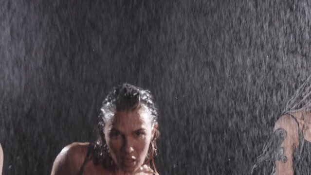 A team of three sexy women with tattoos on their bodies dancing in a dark room in the rain