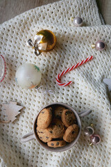 Fototapeta na wymiar Bowl of cookies, soft knitted blanket and colorful Christmas ornaments at home. Flat lay.