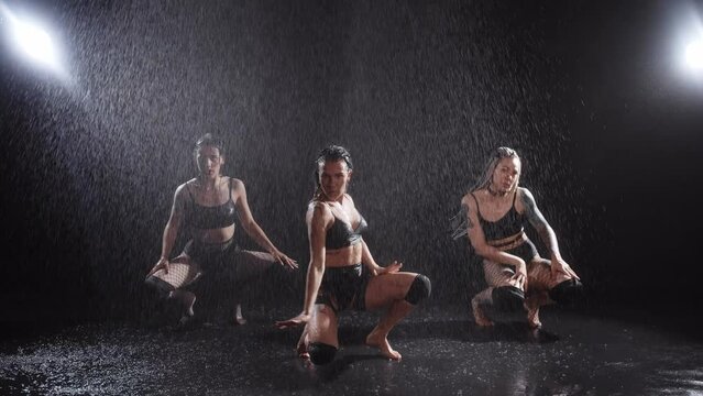 Three attractive sexy women dancing in the dark studio under water splashes