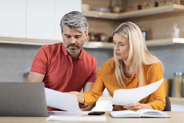 Middle aged husband and wife checking documents, kitchen interior