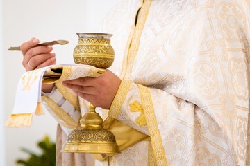 The priest holds in his hands a cup of yellow or gold color with consecrated mysteries. First Communion. Holy Divine Liturgy