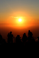 Fototapeta na wymiar silhouettes of people at sunset on the beach. vertical photo of people watching sunset from a mountain above the sea in Greece
