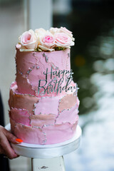 Beautiful two-tier pink cake with rosebuds and the inscription happy birthday. 