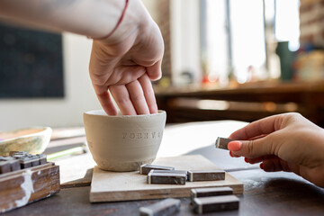 Woman doing pottery on the workshop. Word forever typed on a wet clay.