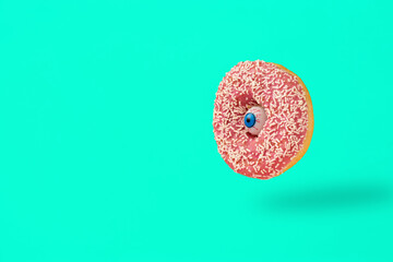 Human eye with Donut composition against a turquoise background. Halloween Santa Muerte and food concept.