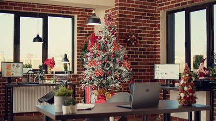 Christmas tree and decorations in company office, festive ornaments and lights to celebrate xmas winter holiday. Empty workplace with seasonal decor for celebration, santa tradition.