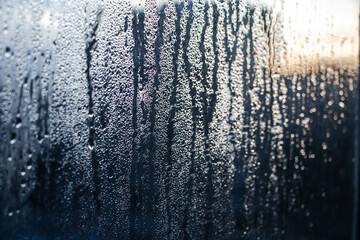 Texture of misted glass in winter. Frozen drops of water in sun on window. Dawn outside window. Abstract background. Selective focus.