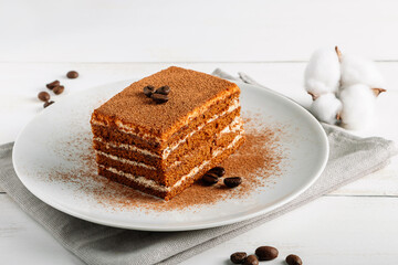 Traditional Italian dessert tiramisu on light background. Tiramisu cake decorated with coffee beans. Slice of coffee cake on white plate.