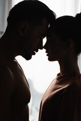 side view of silhouettes of woman in t-shirt and shirtless man standing face to face with closed...