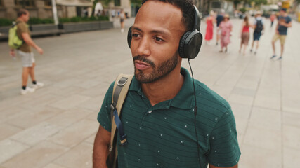 Young man tourist walks around the square of the old city, listens to music in headphones