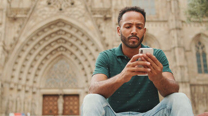 Close up, young man uses cellphone while sitting on the steps of the Sagrada Familia in Barcelona