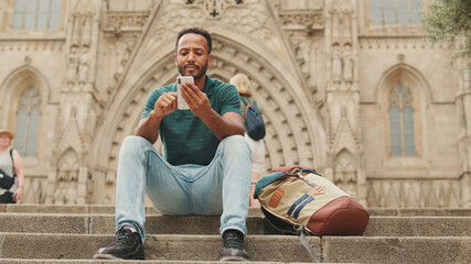 Fototapeta na wymiar Close up, young man uses cellphone while sitting on the steps of the Sagrada Familia in Barcelona