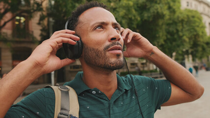 Close up, young man tourist walks around the square of the old city, listens to music in headphones, puts his hands to the headphones