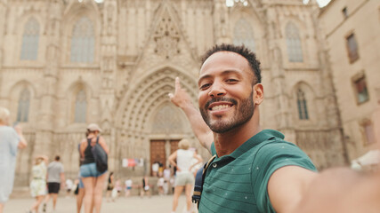 Close-up of young man tourist with backpack on his shoulder taking selfie on the Sagrada Família background
