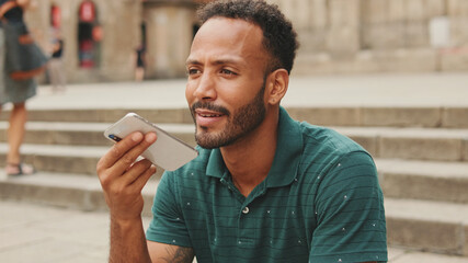 Close up, happy young man sits on the steps of Sagrada Familia in Barcelona, sends voice message...