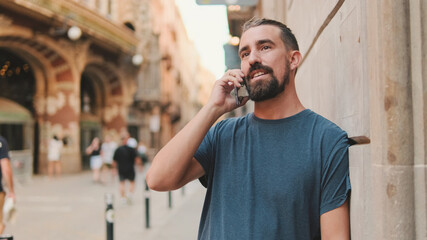 Close-up of young man with beard talking on cellphone against the background of the old city