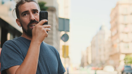 Close-up young man with beard uses cellphone while standing on crosswalk, sends voice message