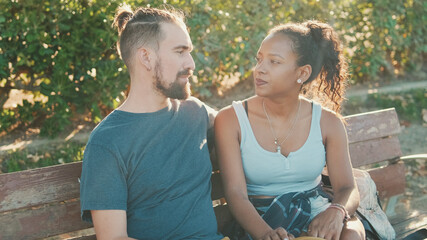 Interracial couple talking while sitting on bench. Backlight