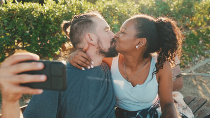 Happy smiling interracial couple kissing while sitting on bench