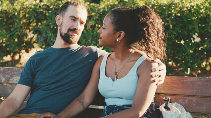 Interracial couple talking while sitting on bench. Backlight