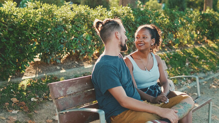 Interracial couple talking while sitting on bench. Backlight