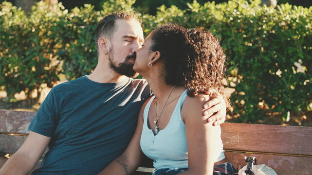 Happy smiling interracial couple kissing while sitting on bench