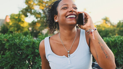 Laughing young mixed race woman sitting on park bench talking on cellphone