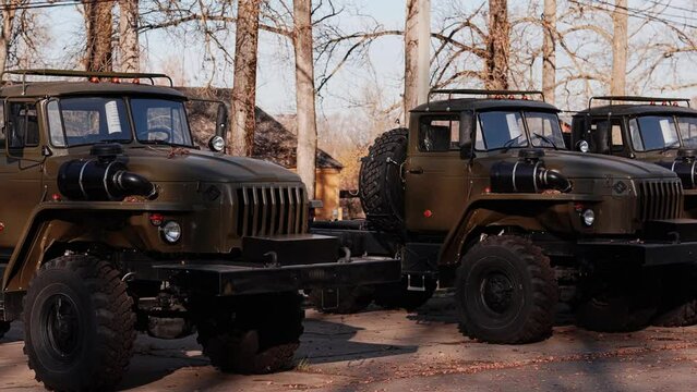 Military trucks of dark green color stand in a row on an asphalt platform. The camera captures a smooth panorama