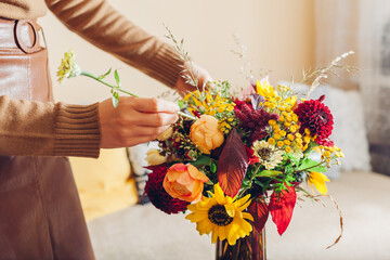 Flower arrangement. Woman makes fall bouquet of sunflowers dahlias roses and zinnias in vase at...
