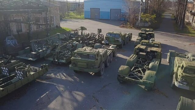 Various types of military equipment stand on the asphalt platform in front of the hangars.