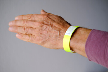 close-up of neon yellow paper bracelet on the male arm of adult clinic patient, check tape with...