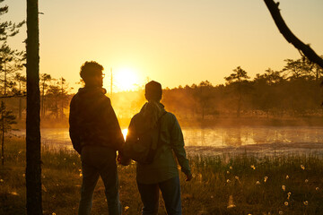 woman and man holds hands tourist meets dawn in nature. Sunset,  light and fog, Reflections of trees in lakes . Travel romance. Viru swamps Estonia.